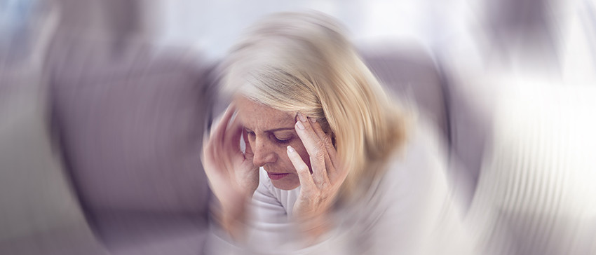 Frau sitzt auf einem Sofa mit Händen an der Schläfe